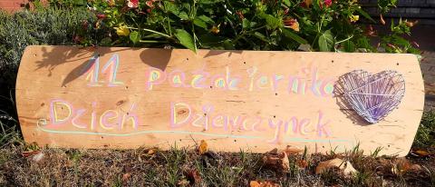 Zdjęcie drewnianej deski na tle trawy z napisem Międzynarodowy Dzień Dziewczynek